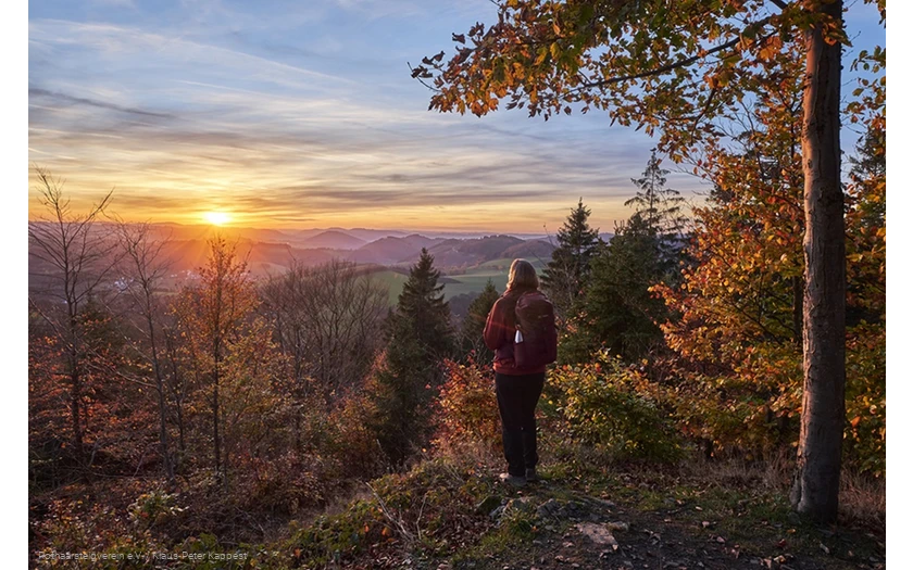 Frau blickt bei Sonnenuntergang über die herbstliche Landschaft am Rothaarsteig