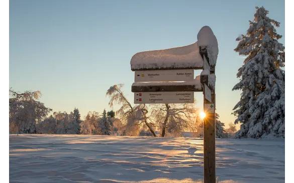 Verschneites Wanderschild am Rothaarsteig im Sonnenlicht