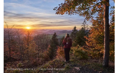 Frau blickt bei Sonnenuntergang über die herbstliche Landschaft am Rothaarsteig