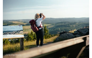 Frau steht auf dem Clemensberg am Rothaarsteig und fotografiert mit einer Kamera die Aussicht