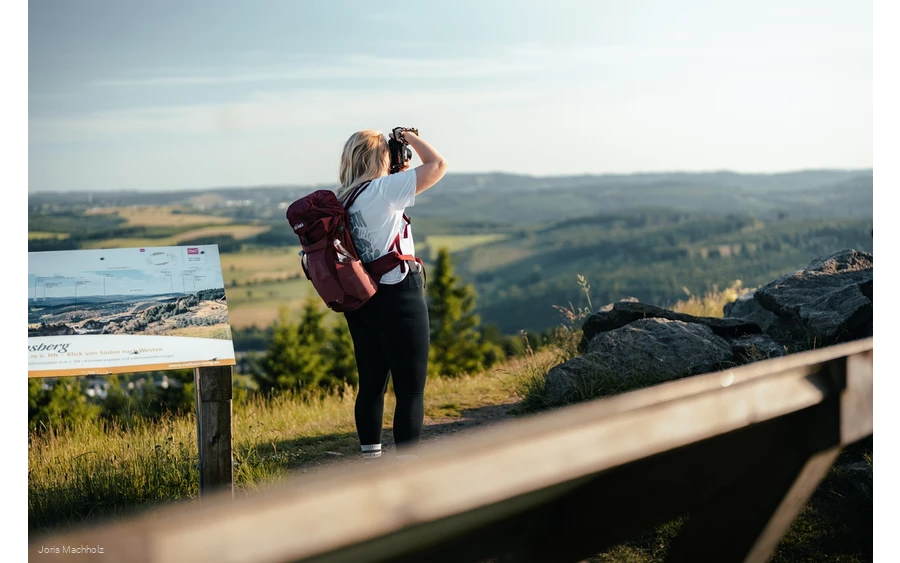 Frau steht auf dem Clemensberg am Rothaarsteig und fotografiert mit einer Kamera die Aussicht