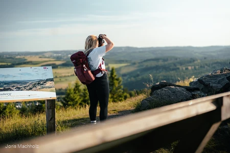 Frau steht auf dem Clemensberg am Rothaarsteig und fotografiert mit einer Kamera die Aussicht