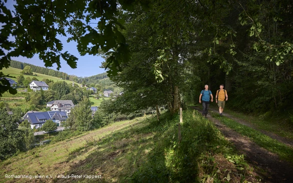 Zwei Wanderer im grünen Wald mit Ausblick auf den Ort Latrop am Rothaarsteig