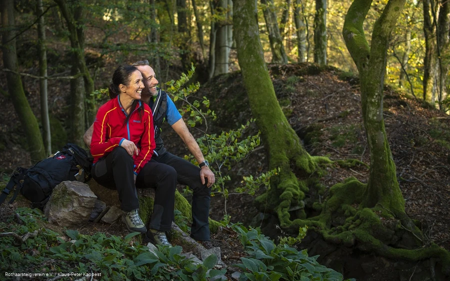 Zwei Rothaarsteig-Wanderer sitzen im grünen Wald auf einem Stein