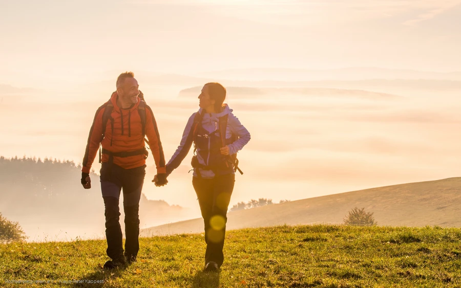 Zwei Rothaarsteig-Wanderer im Sonnenaufgang auf einer Wiese