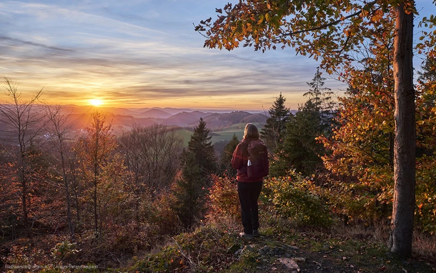 Frau blickt bei Sonnenuntergang über die herbstliche Landschaft am Rothaarsteig