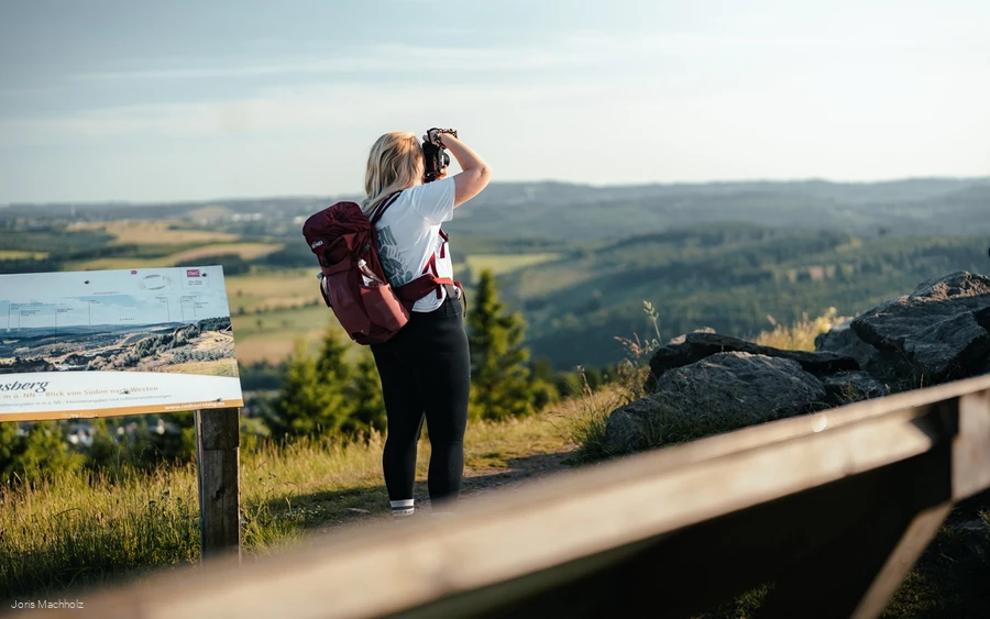 Frau steht auf dem Clemensberg am Rothaarsteig und fotografiert mit einer Kamera die Aussicht