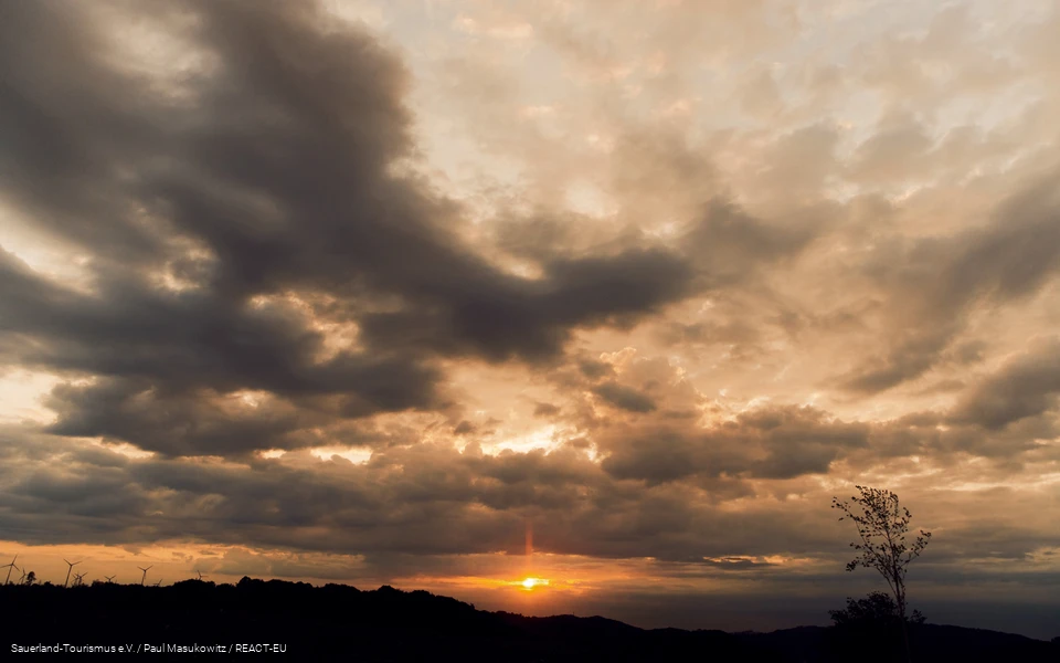 Wolkenverhangener Himmel. Untergehende Sonne scheint durch Lücke in den Wolken.
