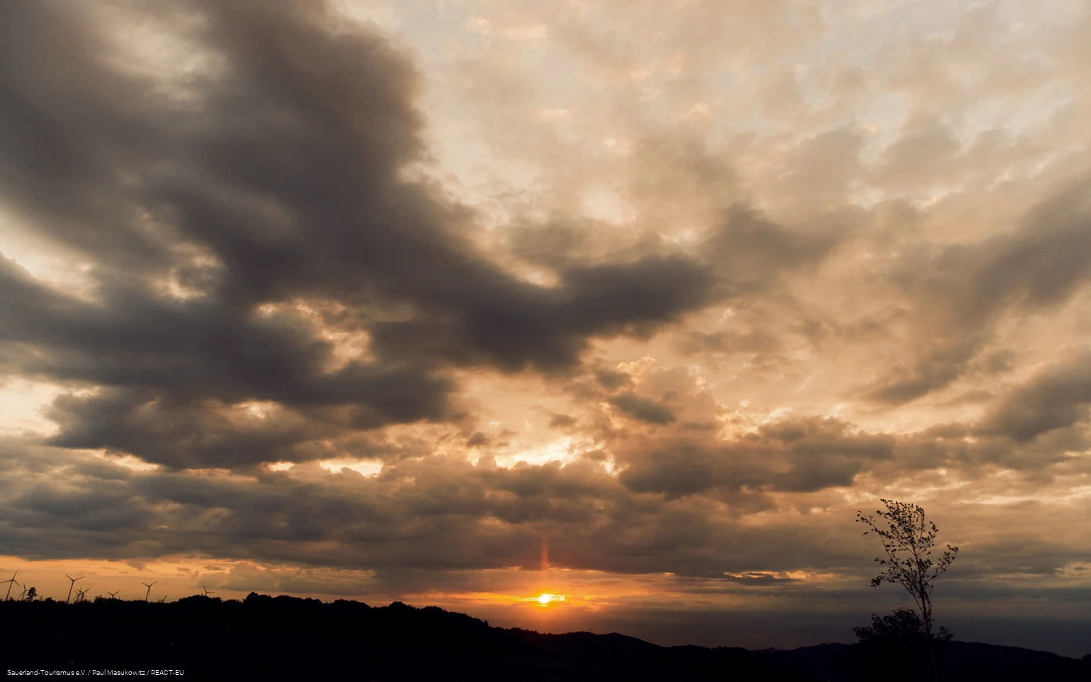 Wolkenverhangener Himmel. Untergehende Sonne scheint durch Lücke in den Wolken.