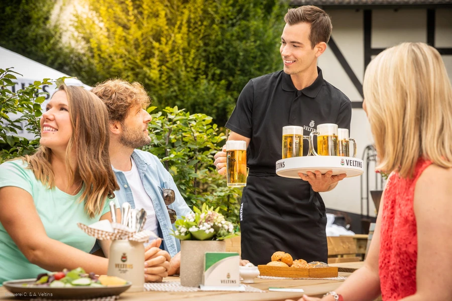 A group is served fresh Veltins at the table outside
