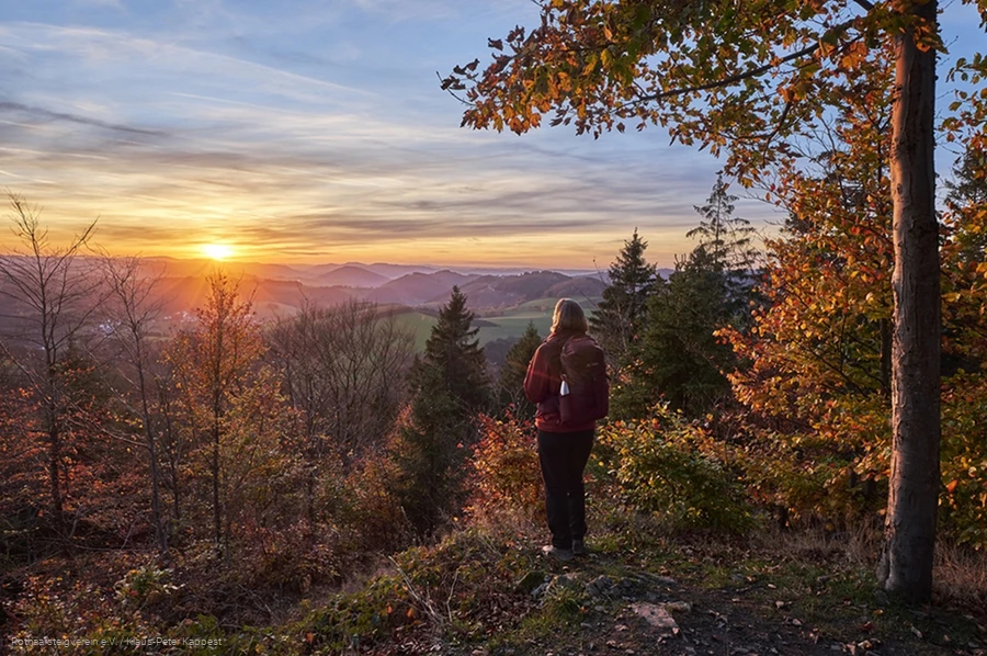 Frau blickt bei Sonnenuntergang &uuml;ber die herbstliche Landschaft am Rothaarsteig
