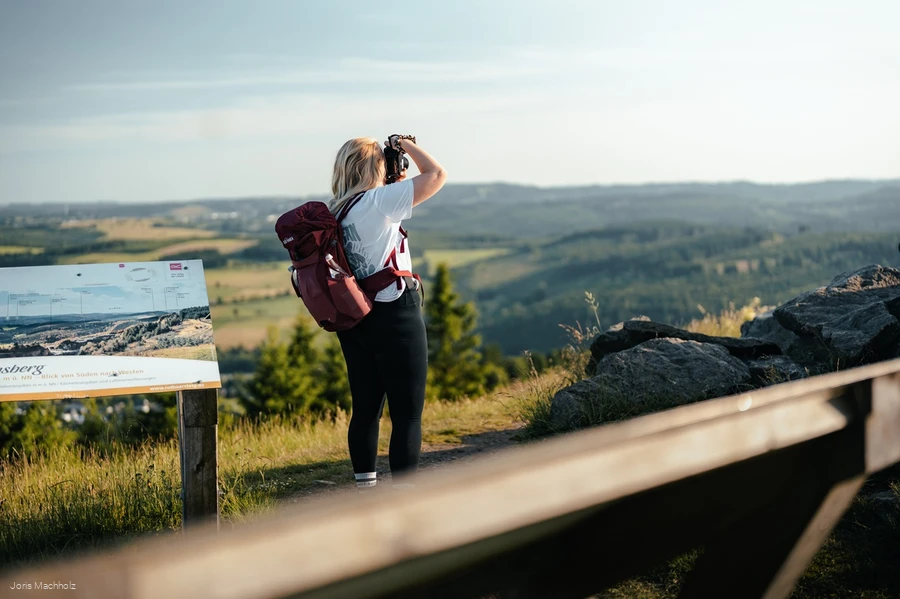 Frau steht auf dem Clemensberg am Rothaarsteig und fotografiert mit einer Kamera die Aussicht