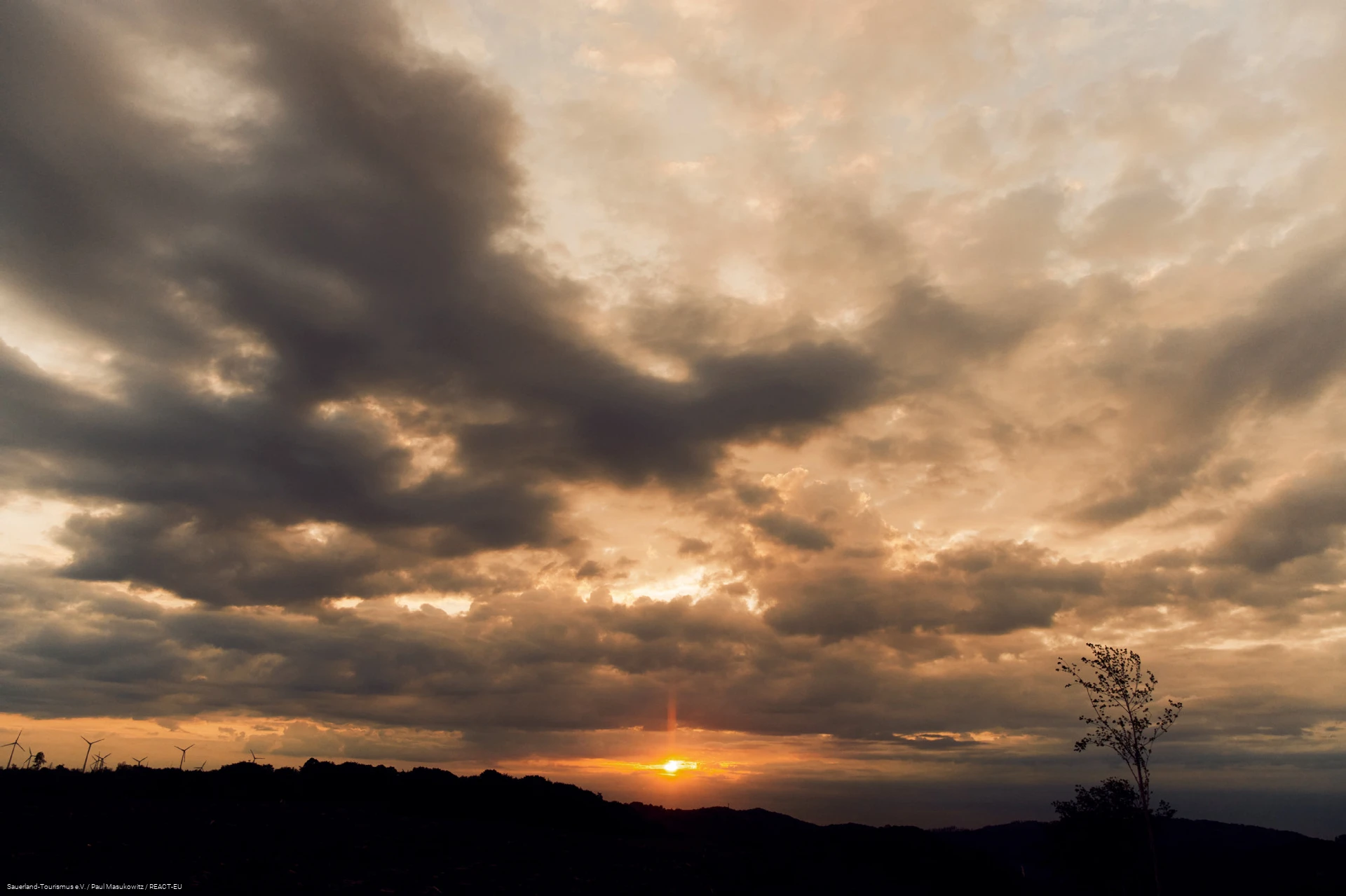 Wolkenverhangener Himmel. Untergehende Sonne scheint durch Lücke in den Wolken.