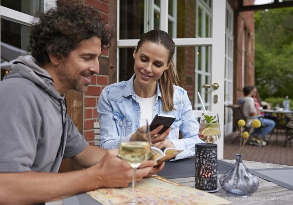 Ein Pärchen sitzt auf der Terrasse bei kalten Getränken und plant eine Wanderung
