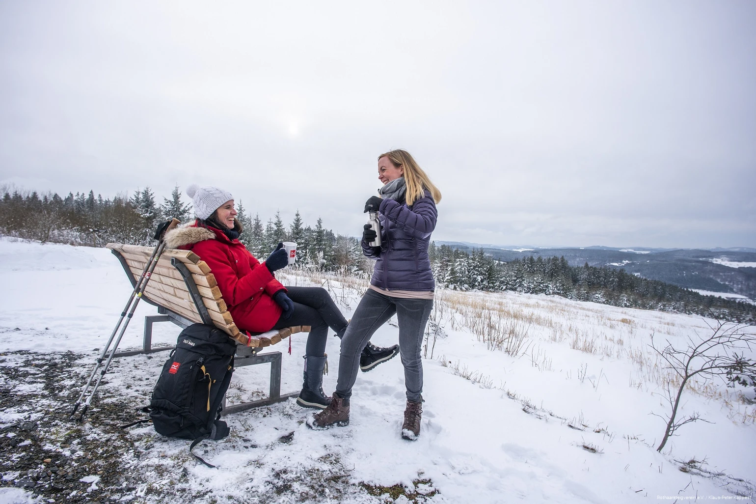 Zwei Frauen machen Pause an einer Rothaarsteig-Waldbank im Schnee