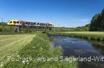 Bahn fährt über einen Fluss durch grüne Landschaft