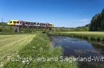 Bahn fährt über einen Fluss durch grüne Landschaft